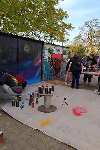 Dziedziniec przed PPM Zajezdnia. Młodzież wspólnie maluje graffiti.